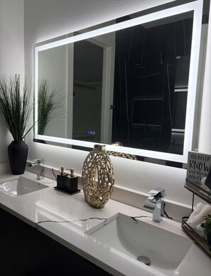 A bathroom with a large mirror, two sinks, a potted plant, a decorative vase, and a sign with a motivational quote. - LuxeStay Townhome 5min from Downtown Dallas (Dallas)