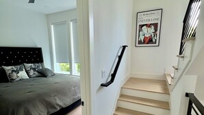 A modern bedroom with a bed, a ceiling fan, and a staircase with a handrail. - LuxeStay Townhome 5min from Downtown Dallas (Dallas)