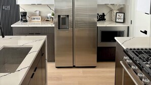 A modern kitchen with a stainless steel refrigerator, a gas stove, and white cabinetry. - LuxeStay Townhome 5min from Downtown Dallas (Dallas)