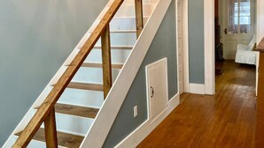 Una escalera con barandillas de madera y un candelabro, que conduce a una habitación con una puerta y una ventana.