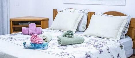 A neatly made bed with floral bedding, a bedside table with a lamp, and a mirror on the wall.