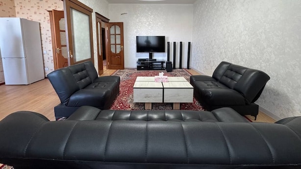 Un salon avec un grand canapé en cuir noir, une table basse blanche et un téléviseur à écran plat.