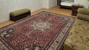 Une pièce avec un grand tapis à motifs, un banc, un lit, une petite table et un luminaire suspendu.