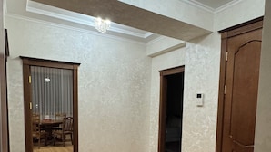 Une pièce spacieuse avec un plancher en bois, un tapis à motifs, un lustre et une porte.