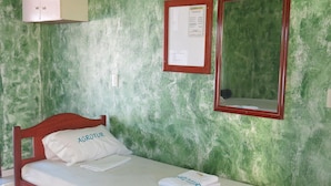 A single bed with a wooden frame, a white mattress, and a pillow with "AGROTUR" written on it. There is a folded towel on the bed, and a mirror with a red frame is mounted on the wall. - Hotel Agrotur (Manaus)