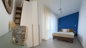 A bedroom with a bed, a wardrobe, a desk with a sign, a mirror, and a blue accent wall. - Mediterranea Suite holiday home (Gela)