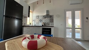 A modern kitchen with a black refrigerator, a wooden table with a red and white ring buoy, a tiled backsplash, and a sliding glass door leading to an outdoor area. - Mediterranea Suite holiday home (Gela)