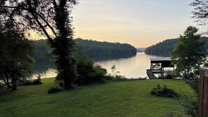 A grassy area with a wooden deck overlooking a lake, surrounded by trees. - Charming 3-beds with loft in peaceful cove on Watts Bar Lake! Bring your boat! (Ten Mile)