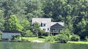 A house with a large deck and a dock extending into a lake, surrounded by dense trees. - Charming 3-beds with loft in peaceful cove on Watts Bar Lake! Bring your boat! (Ten Mile)