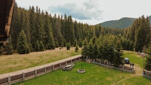 A fenced outdoor area with a circular fire pit, surrounded by a wooden deck and a stone wall. - CABANA LAPTICI (Moroeni)