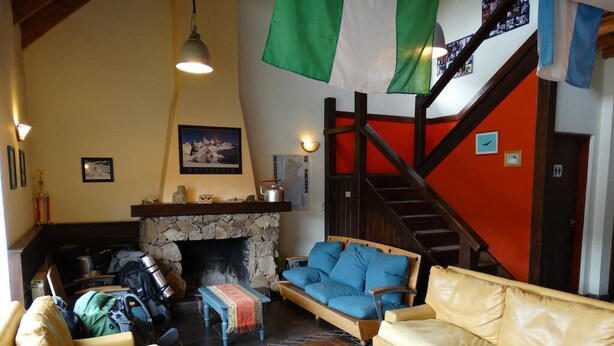 A cozy living room with a stone fireplace, a wooden staircase, and a sofa with blue cushions. - Condor de los Andes (El Chalten)