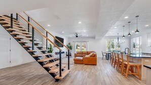 A modern interior with a wooden staircase, a living room with a sofa, and a kitchen area.