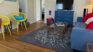 Ein Wohnzimmer mit einem blauen Sofa, gelben Sesseln, einem Couchtisch und einem Fernseher auf einem Schrank.