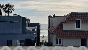 Ein Küstengebäude mit Balkon mit Blick auf den Strand, eine Palme und freie Sicht auf das Meer.