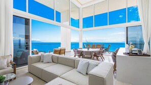 Un intérieur moderne avec un grand canapé, une table à manger et des chaises, offrant une vue imprenable sur l’océan.