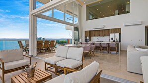 A modern open-plan living area with a view of the sea, a kitchen, and a dining area with outdoor seating.