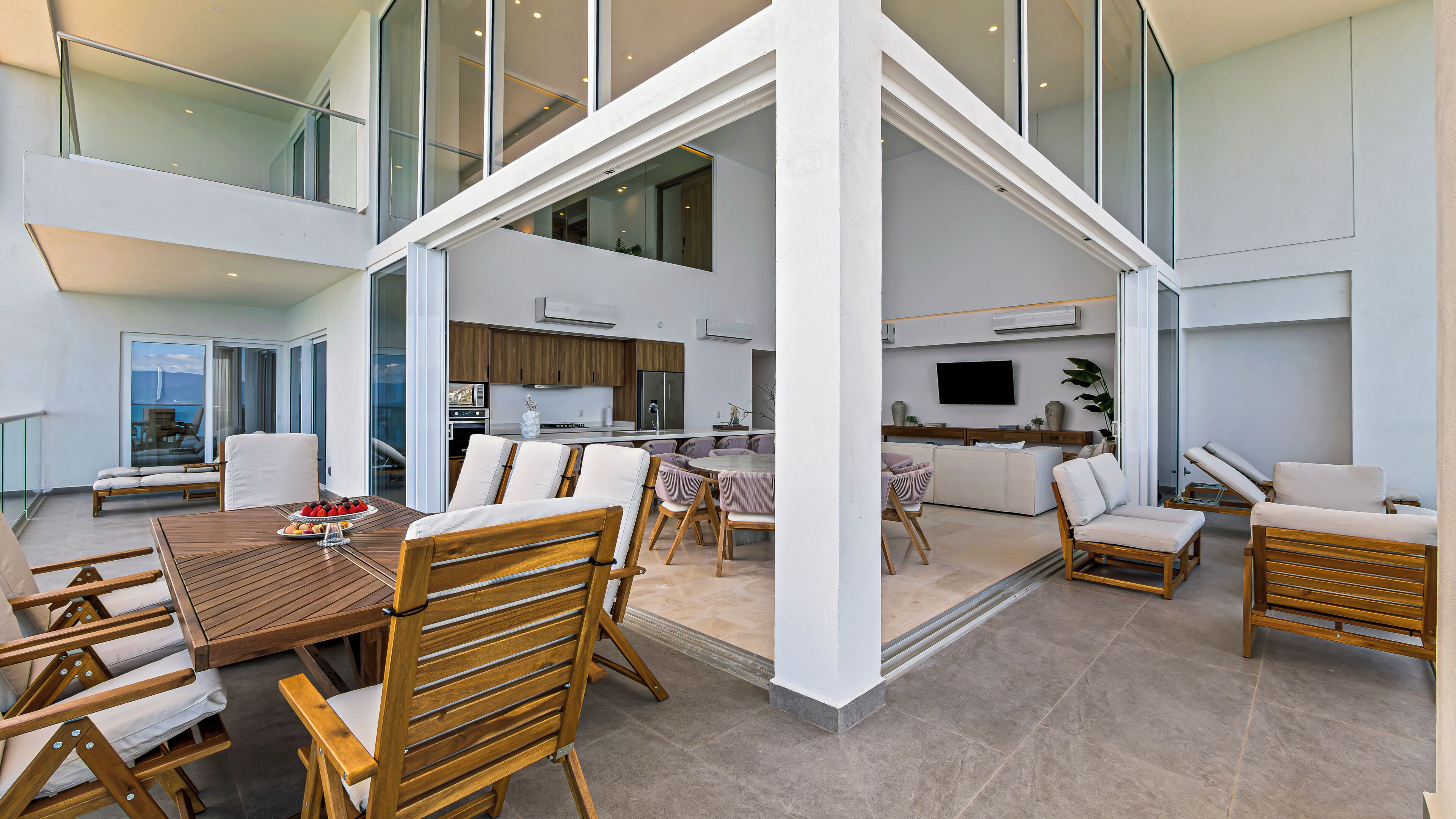 A spacious open-plan living area with a dining table, multiple seating options, a kitchen, and a large TV.