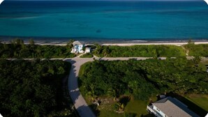 Vista aerea di una proprietà costiera con una strada che conduce a una casa, immersa nel verde e con una spiaggia sullo sfondo.