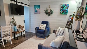 Un soggiorno con una poltrona blu, un divano, una televisione, un quadro e una ghirlanda decorativa.