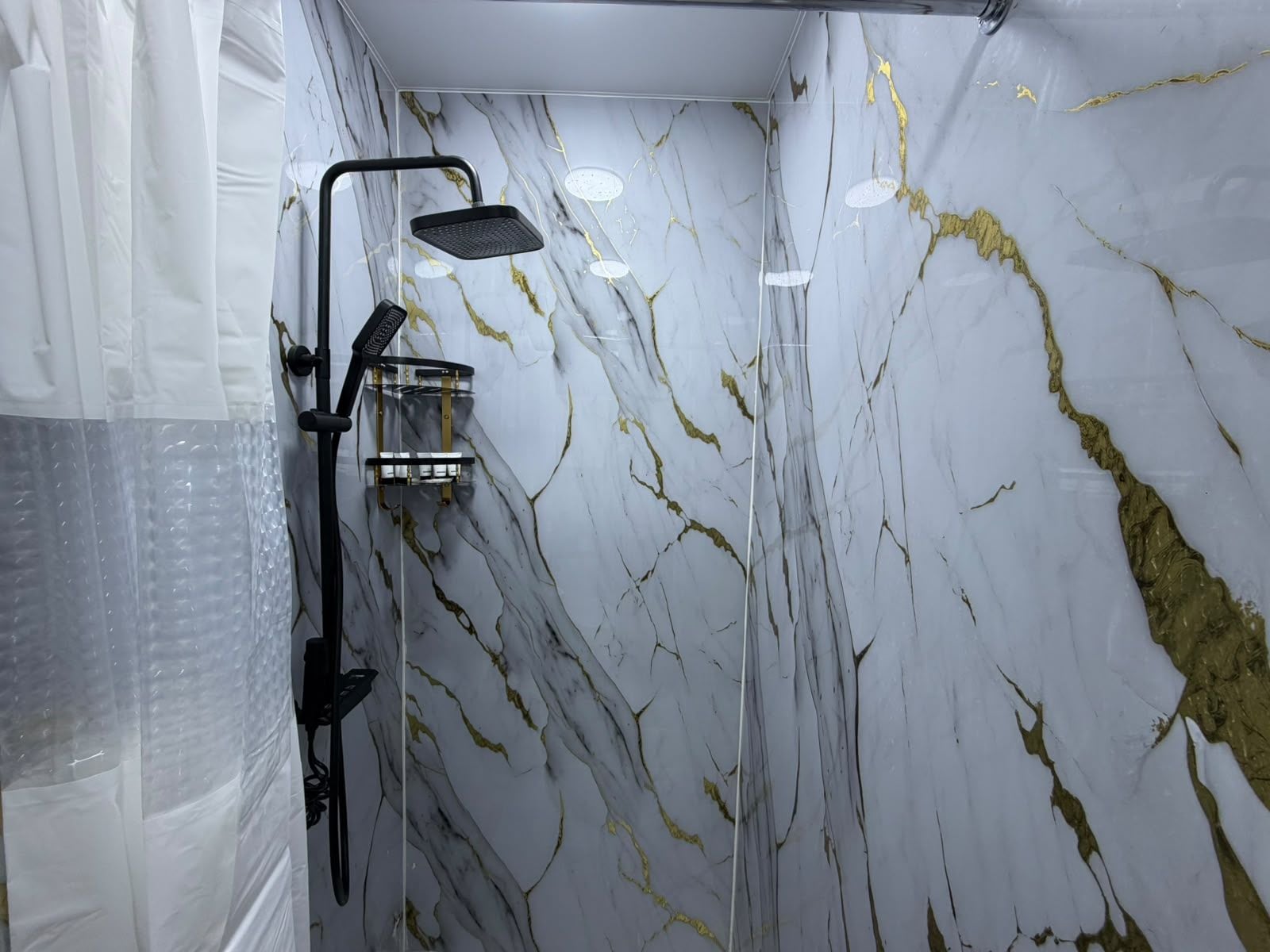 A bathroom with a shower, marble walls, and a glass partition.