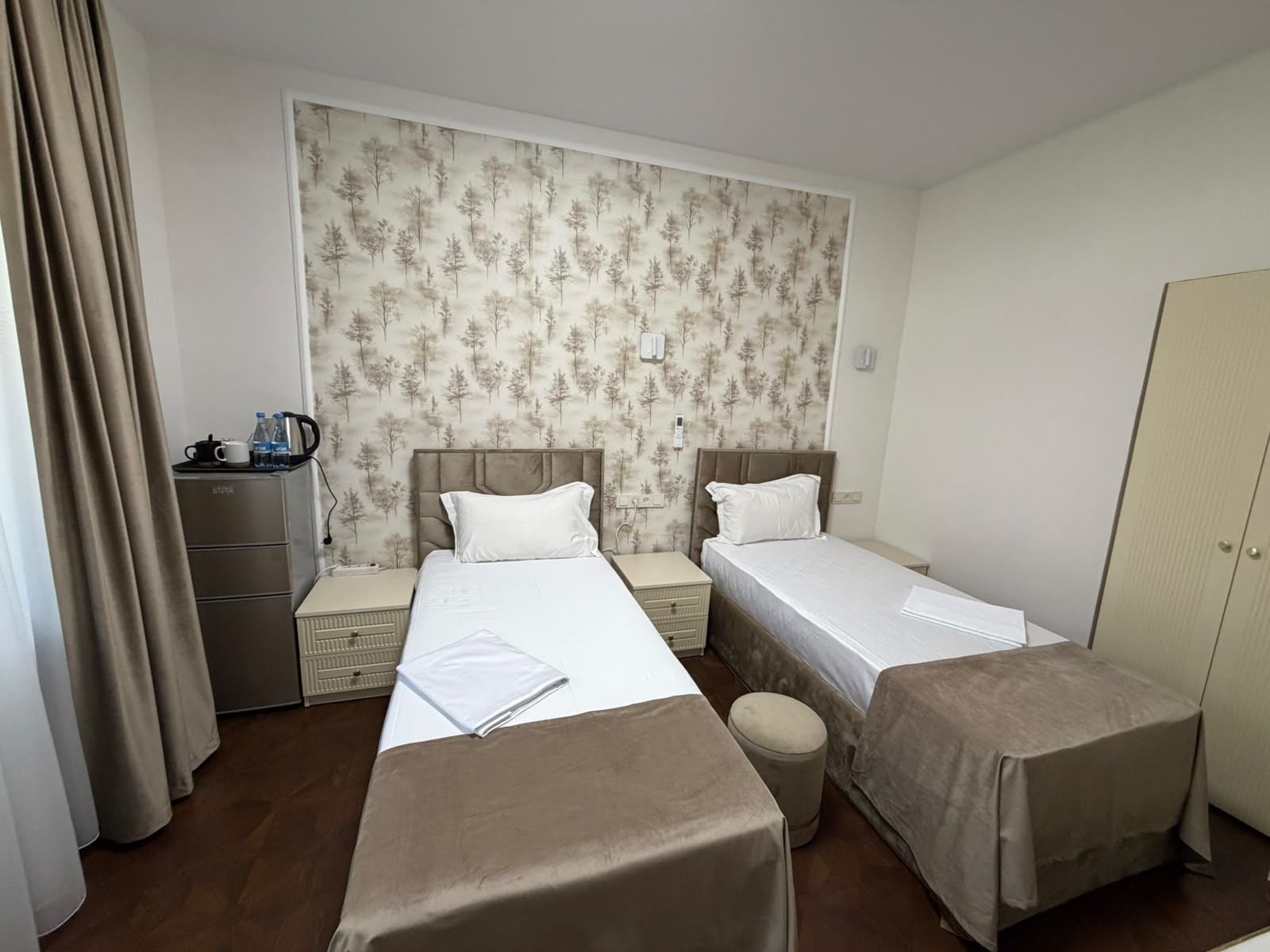 A hotel room with two single beds, a small table, a wardrobe, and a radiator.