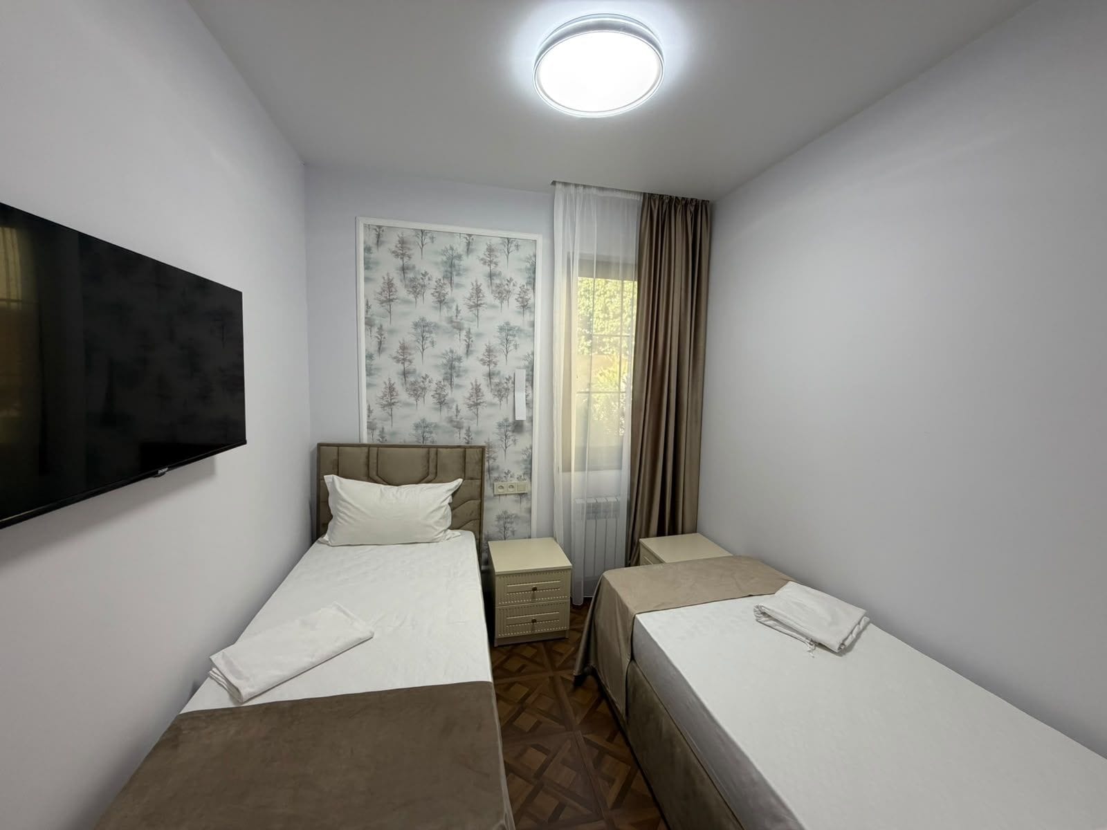 A hotel room with two beds, a TV, a window with curtains, and a radiator.