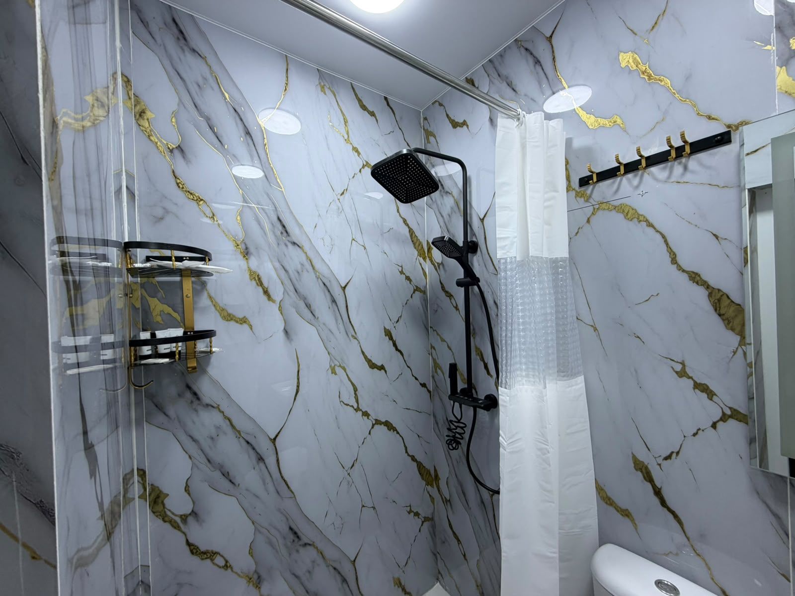 Un baño con pared de mármol, ducha con cabezal de ducha manual y un perchero.