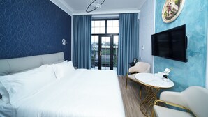Ein Hotelzimmer mit einem großen Bett, einem runden Tisch mit Stühlen, einem an der Wand befestigten Fernseher und Blick auf die Stadt durch das Fenster.