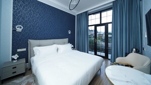 Ein modernes Schlafzimmer mit einem großen Bett, einem Nachttisch, einem Sessel und Blick ins Freie durch ein großes Fenster.