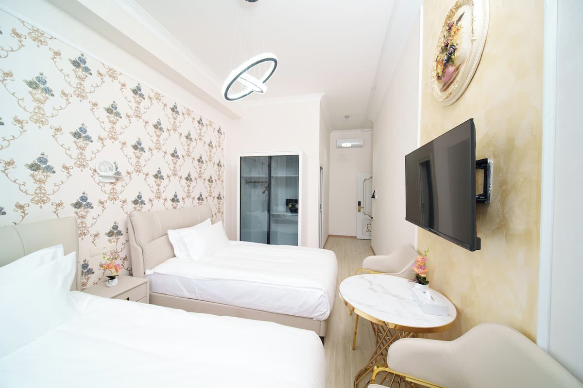 A hotel room with two beds, a small round table, a TV mounted on the wall, and a mirror.