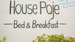 Un mur sur lequel on peut lire « Karibu House Paje » et qui est orné d’un symbole représentant un palmier, indiquant qu’il s’agit d’un établissement proposant des chambres et le petit-déjeuner.