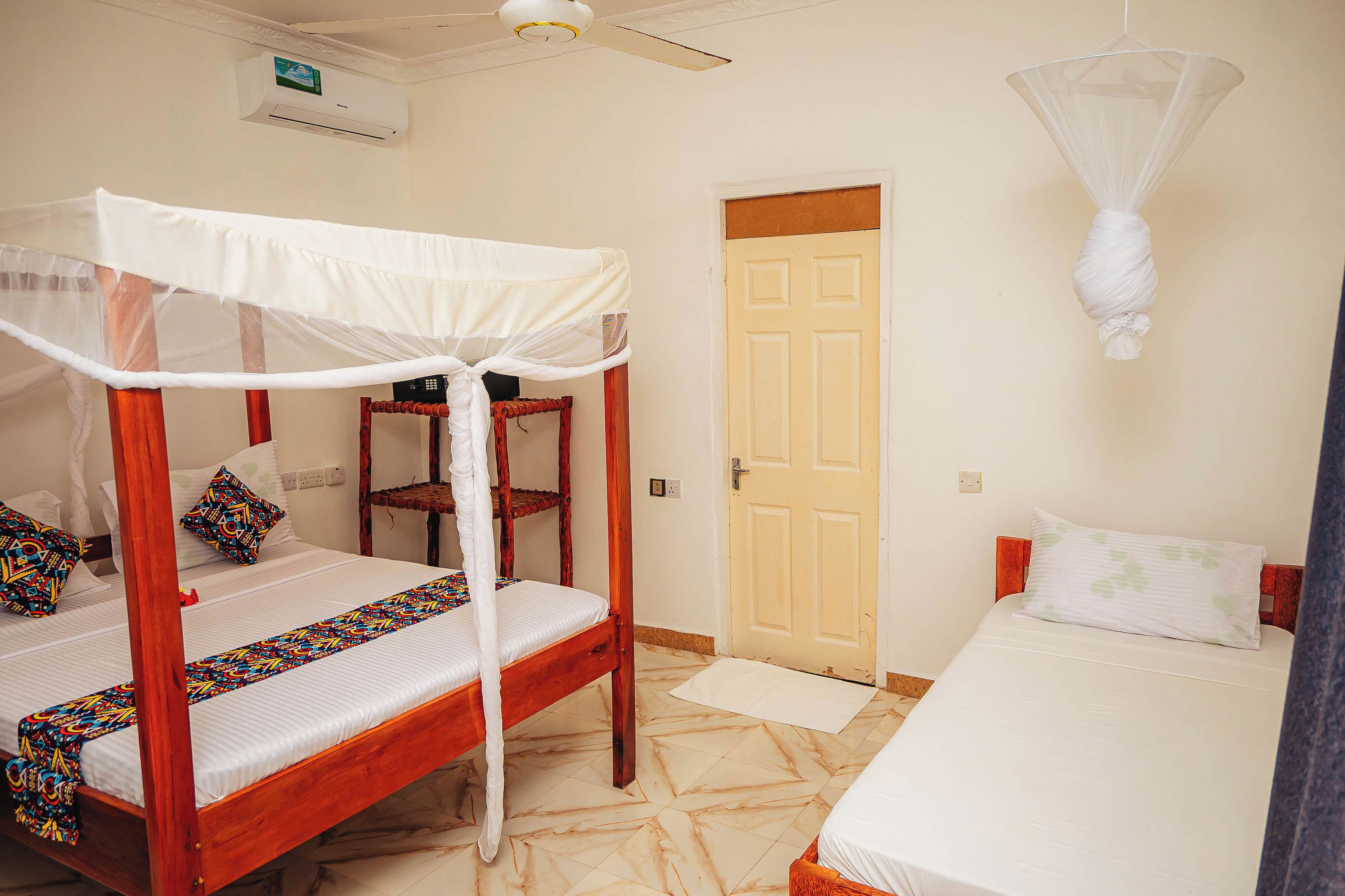 A room with a four-poster bed, a single bed, a door, and a ceiling fan.