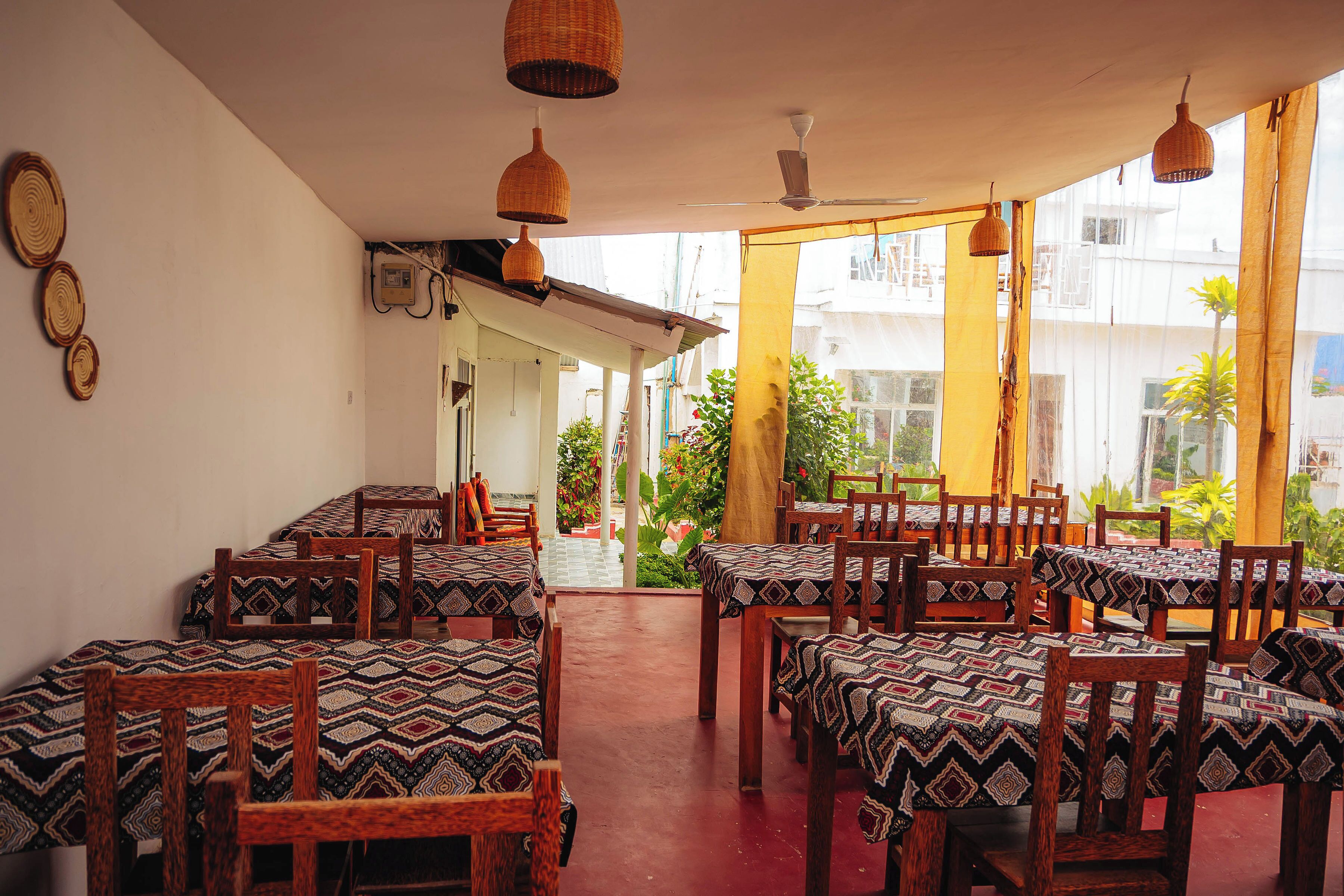 A restaurant with tables covered in patterned tablecloths, wooden chairs, and hanging wicker lamps.