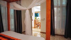 Une chambre à coucher avec un lit, un baldaquin et une vue sur un espace extérieur aménagé avec une chaise et une table.