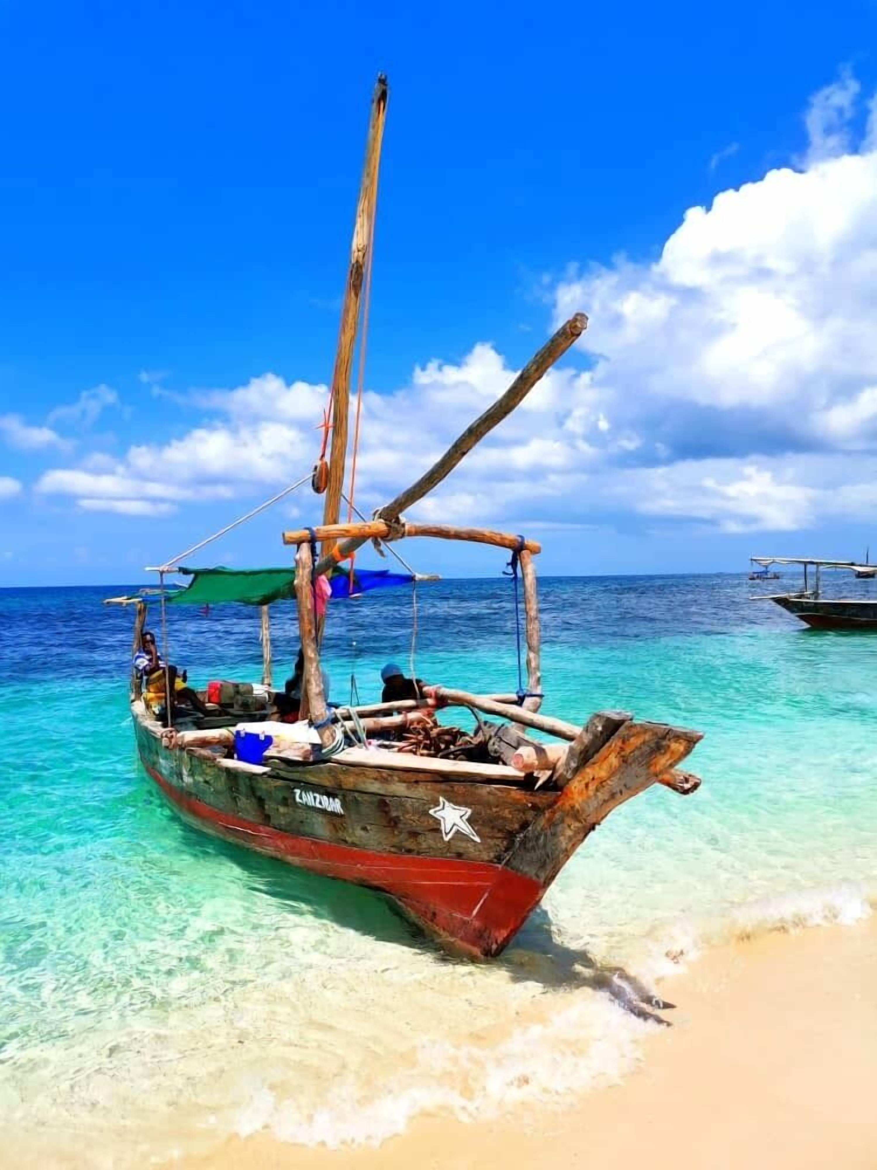 A wooden boat with a star emblem on the side, anchored on a sandy beach with clear turquoise water.
