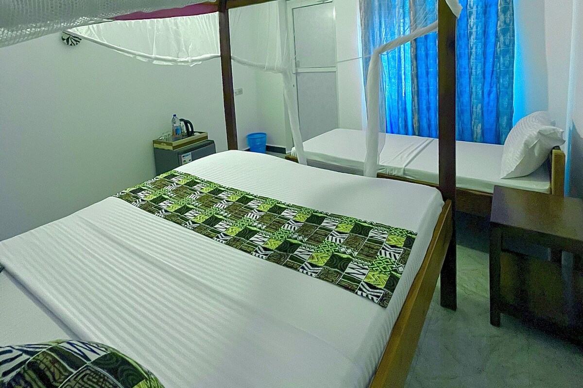 Una habitación con cama, mesita de noche, silla y ventana con cortinas.