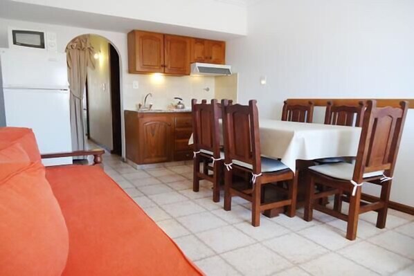 A compact kitchen with wooden cabinets and a dining table with chairs. - Gemelos Apart (Villa Gesell)