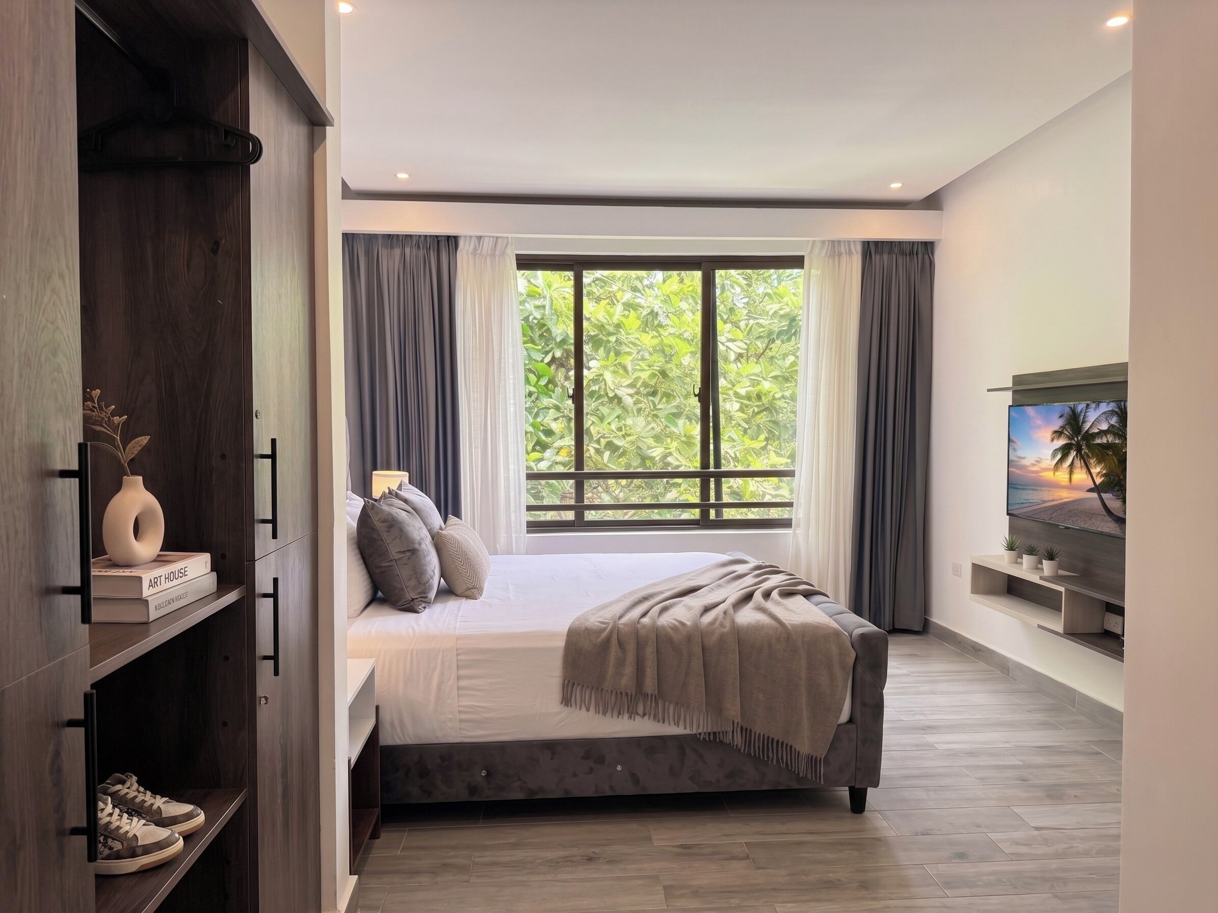 Een moderne slaapkamer met een groot bed, een kledingkast, een televisie en een raam met gordijnen.