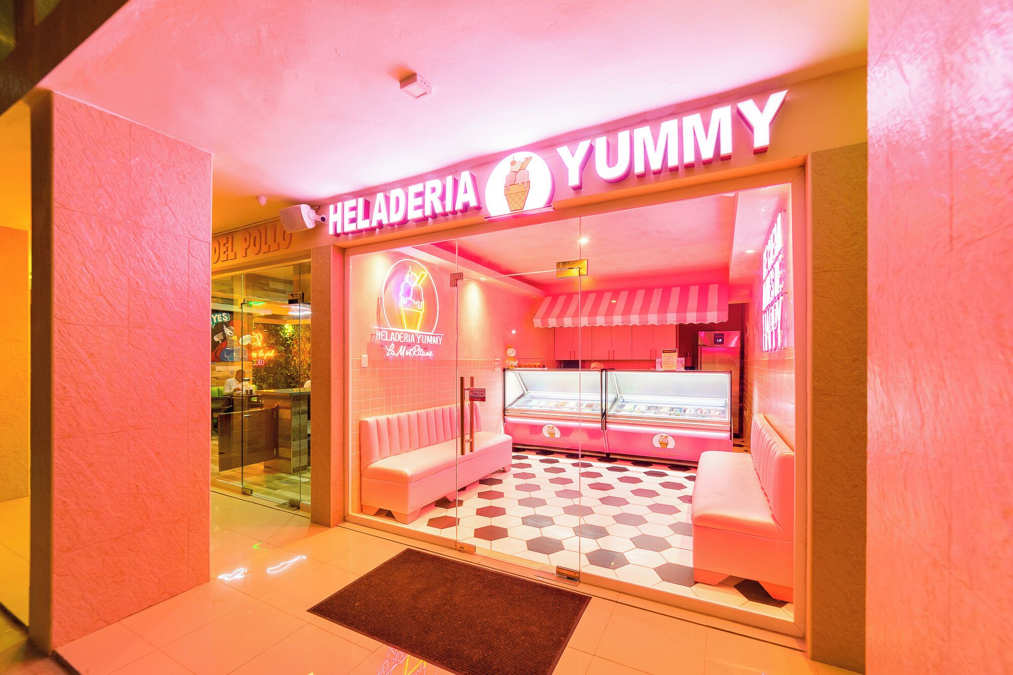 Uma gelataria com tema rosa chamada 'Heladería Yummy', com vitrine de vidro e área de estar.