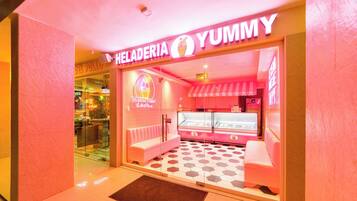 Uma gelataria com tema rosa chamada 'Heladería Yummy', com vitrine de vidro e área de estar.