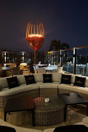 A rooftop lounge with a modern glass balustrade, a central decorative light fixture, and a seating area with sofas and tables. - Hotel Neon (Punta Cana)