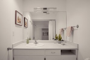 Une salle de bain moderne avec un meuble-lavabo blanc, un grand miroir, un évier et un espace douche.