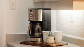 A kitchen with a coffee maker, a mug, and a small plant on the counter. - Spacious 2-Bedroom Condo in Downtown Victoria (Victoria)