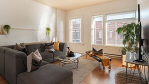 A modern living room with a grey sofa, a glass coffee table, and a large plant. - Spacious 2-Bedroom Condo in Downtown Victoria (Victoria)