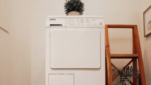 A stacked washer and dryer unit with a wooden ladder and a shelf holding towels and cleaning supplies. - Spacious 2-Bedroom Condo in Downtown Victoria (Victoria)