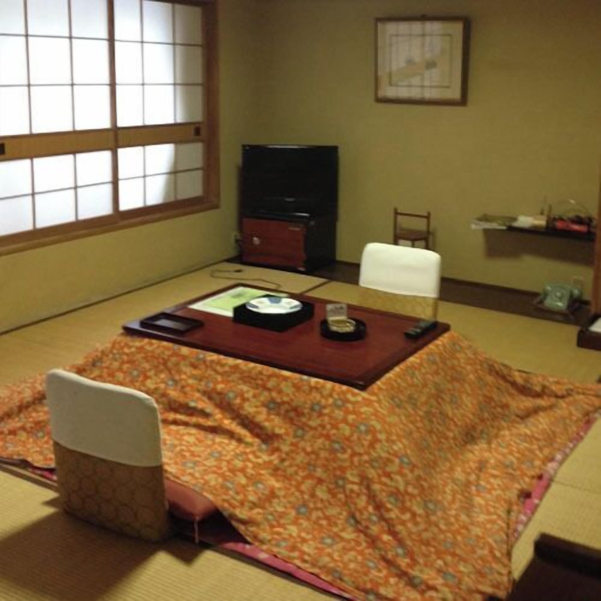 A tatami mat room with a low table, a television, a chair, and a shelf with items.