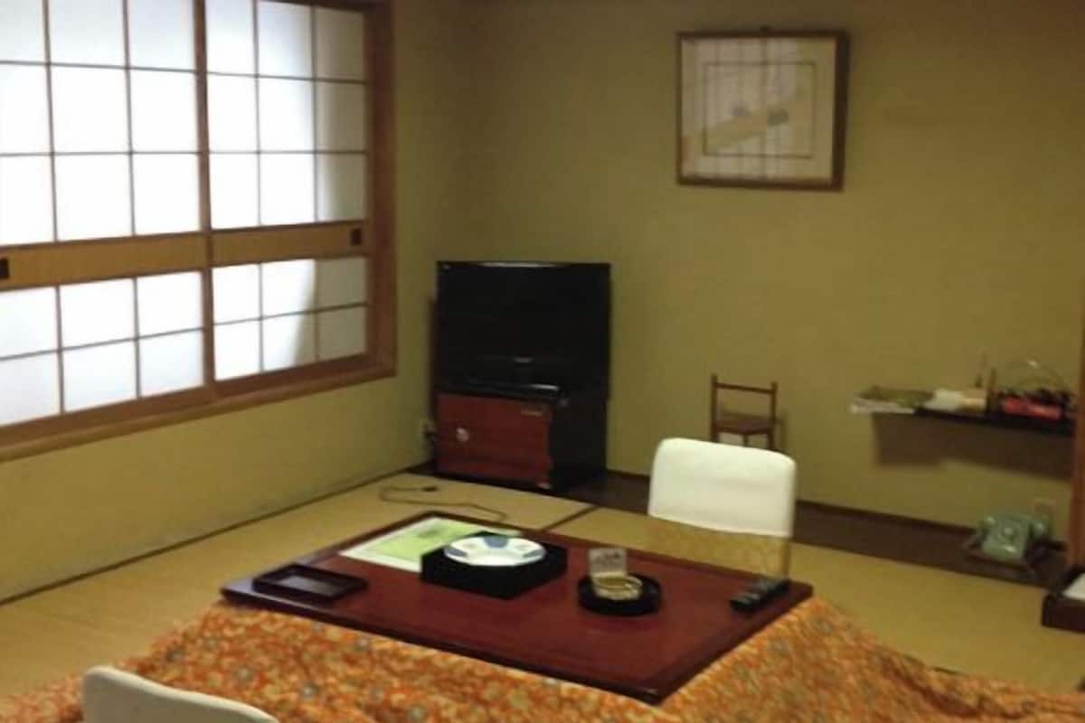 A tatami mat room with a low table, a television, a chair, and a shelf with items.