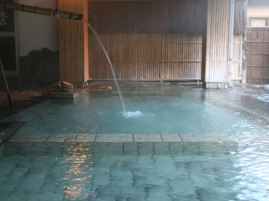 A traditional Japanese onsen with a wooden floor, bamboo walls, and a wooden door.
