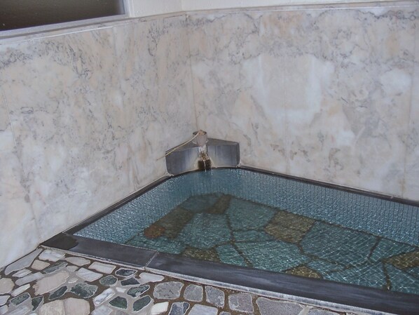 Um canto de um quarto com piso de azulejos, parede de mármore e parte de uma banheira.