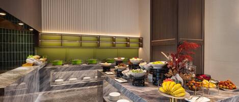 Montaje de bufé con diversos alimentos y platos, una encimera de mármol y una pared verde con líneas verticales.